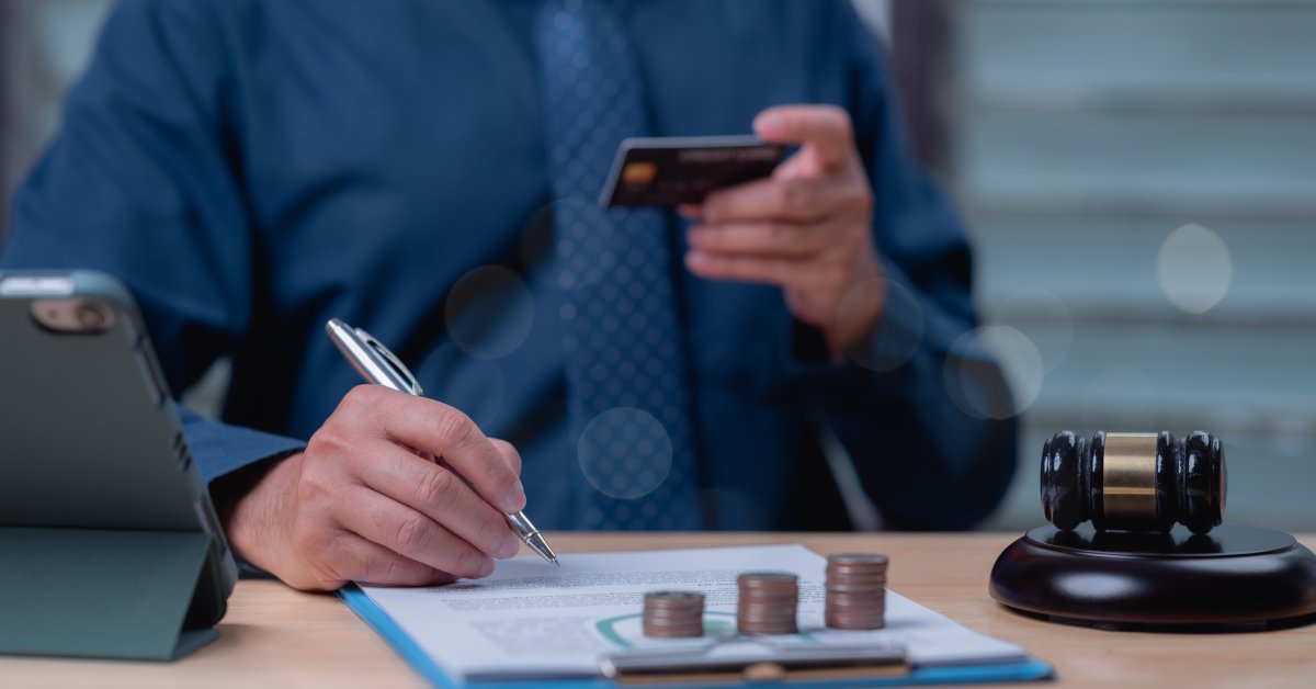 A close-up of a man holding a credit card and writing something down on a clipboard with coins stacked on it.